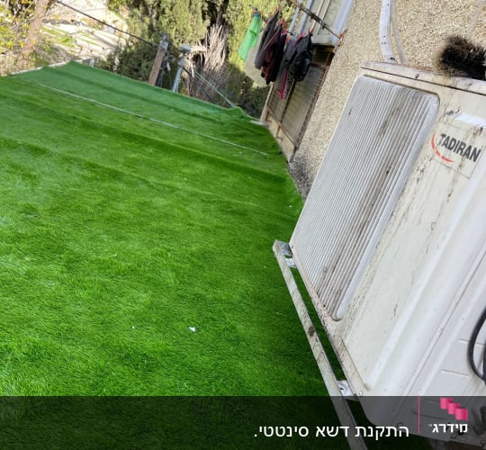 דשא סינתטי ירוק ליד קיר חיצוני של בית